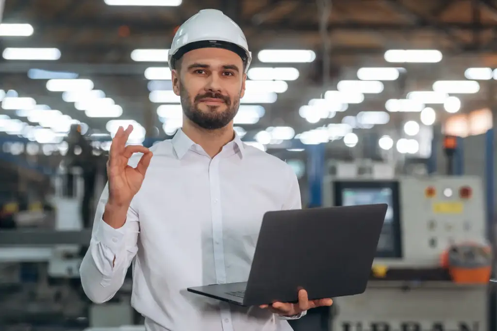 Desarrollo de prototipos industriales personalizados 5 Ingeniero industrial satisfecho con casco y laptop en fábrica moderna